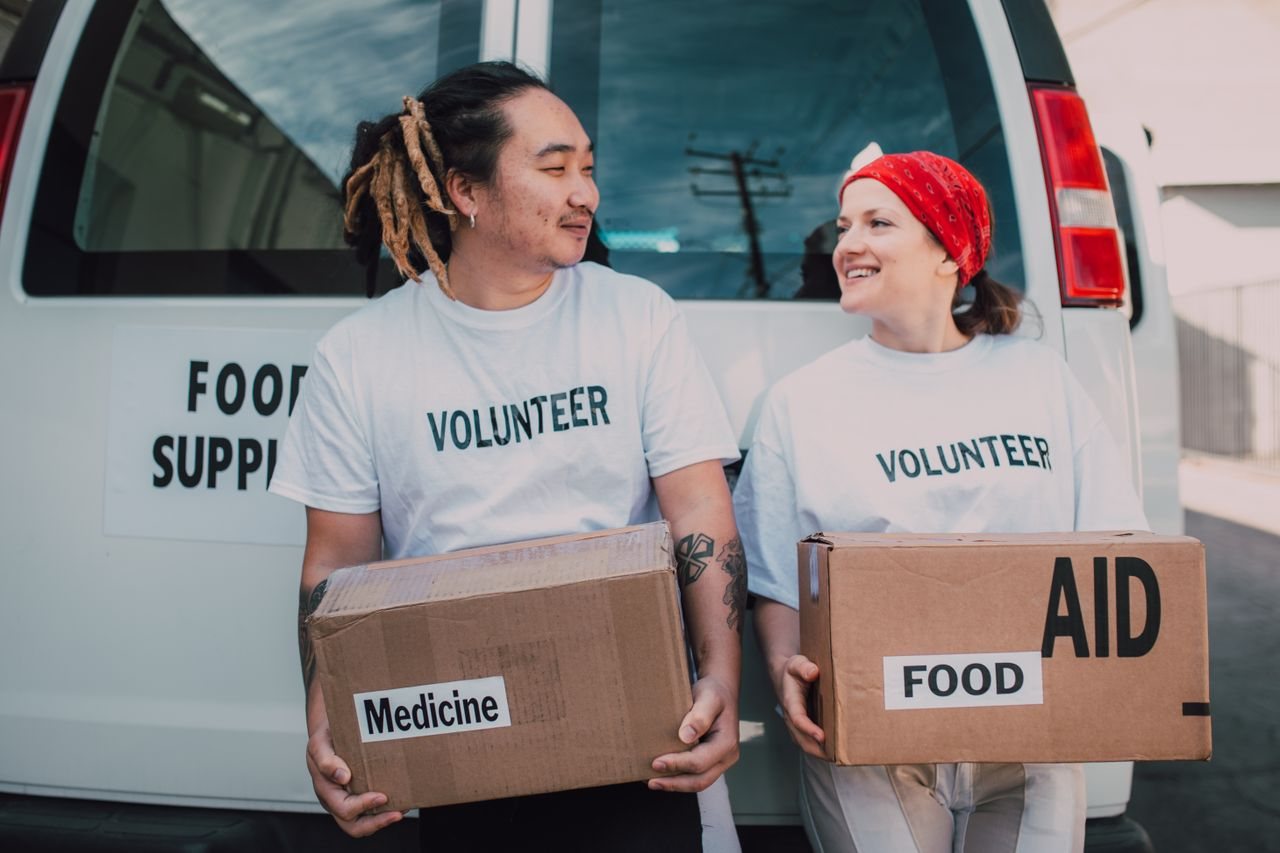 Free Two smiling volunteers carrying boxes labeled food and medicine by a supply van. Stock Photo