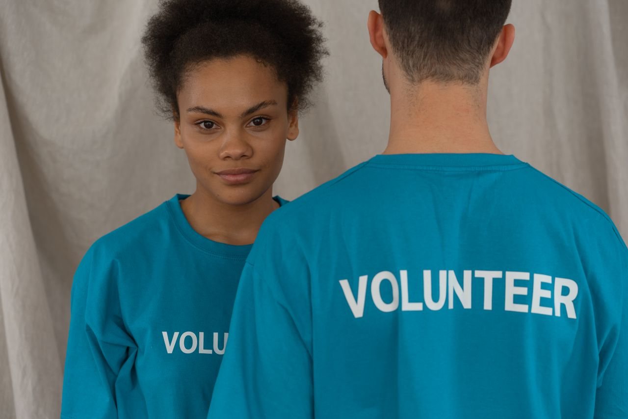 Free Two volunteers in blue shirts, one smiling and facing camera, promoting support and teamwork. Stock Photo