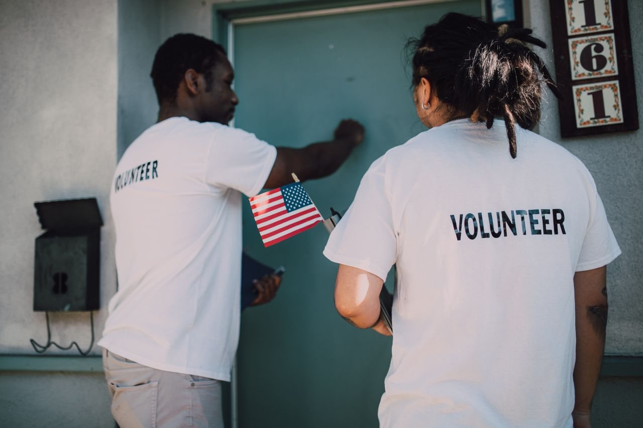 Free Two volunteers knocking on door during a community outreach event, holding a small American flag. Stock Photo