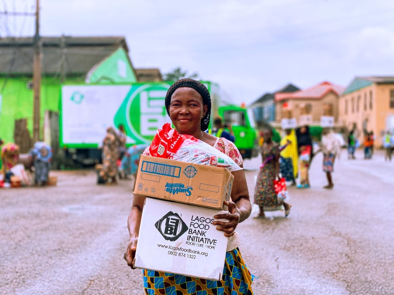 Free Smiling woman holding a food box from Lagos Food Bank on a busy street in Lagos, Nigeria. Stock Photo