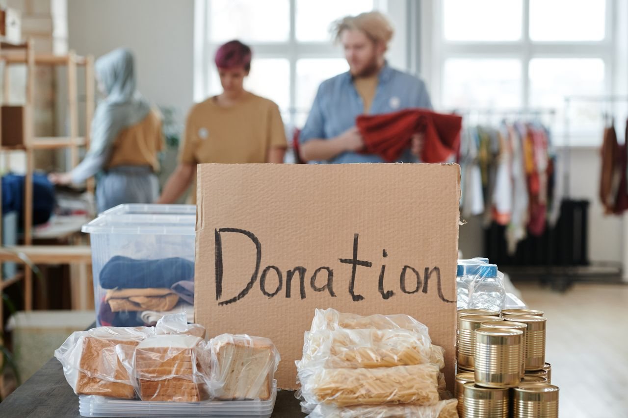 Free Volunteers sort clothes and food in a donation center. Cardboard sign reads 'Donation.' Stock Photo